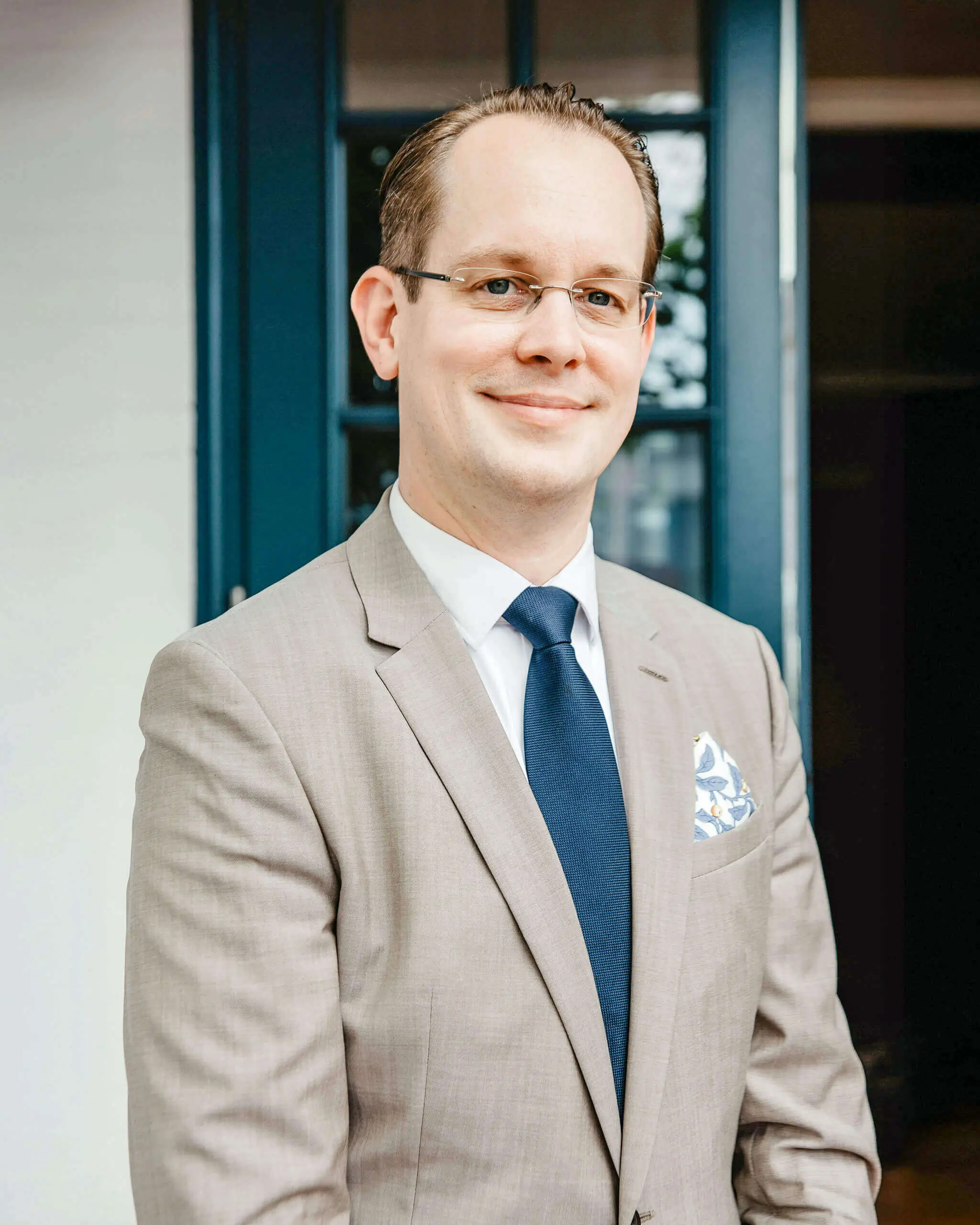 Ein lächelnder Mann in einem Anzug steht vor einer Tür.