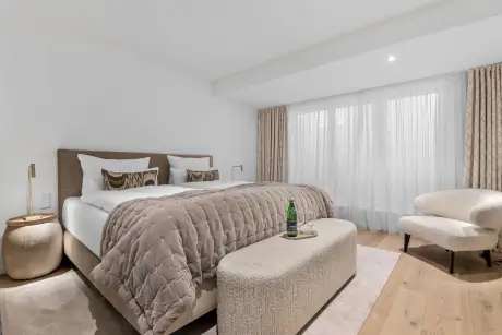 Gemütliches Hotelzimmer mit Bett, stilvollem Stuhl und natürlichem Licht durch das große Fenster.