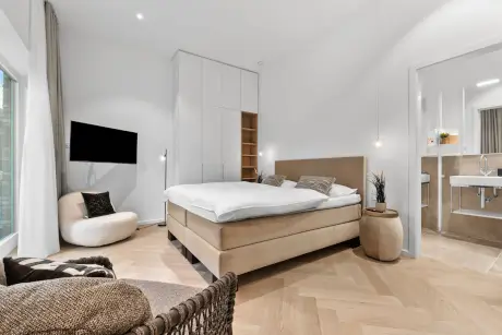 Modernes Hotelzimmer mit Doppelbett, Fernseher und stilvollem Sessel für einen komfortablen Aufenthalt.