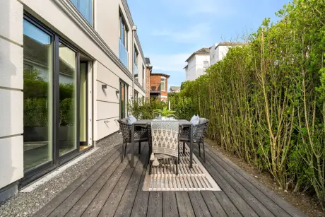 Gemütlicher Essbereich im Freien mit Tisch, Stühlen und grüner Hecke.