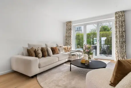 Helles Wohnzimmer mit beige Sofa, schwarzem Couchtisch und frischen Blumen im Hotel Stadt Hamburg.